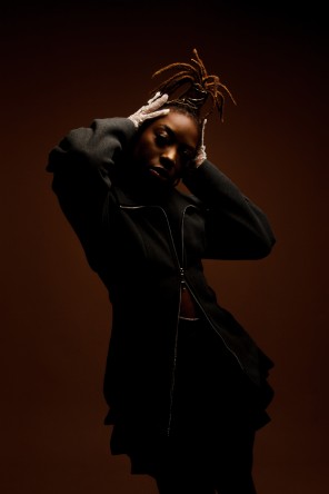 L'artiste Hendrickx Ntela prenant la pose, les mains au niveau du visage